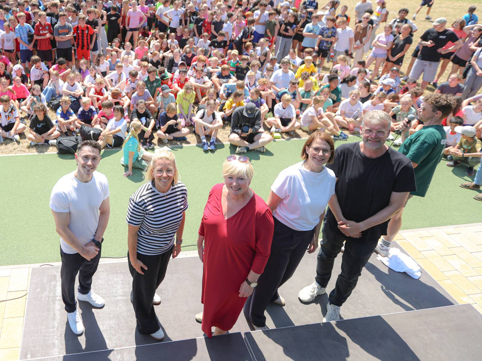 Vier Personen auf einer Bühne. Im Hintergrund sehr viele Kinder.