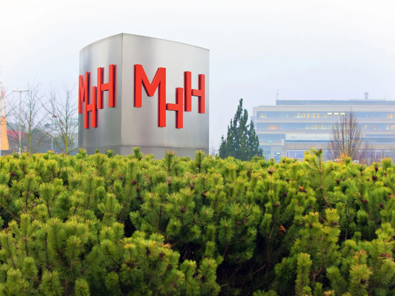 Eine Säule mit den Buchstaben "MHH", im Hintergrund Gebäude.