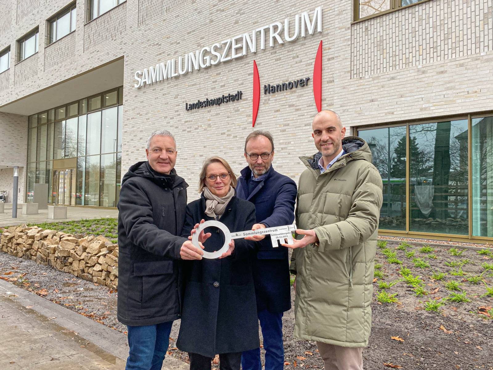 Vier Personen mit einem Schlüssel vor einem Gebäude.