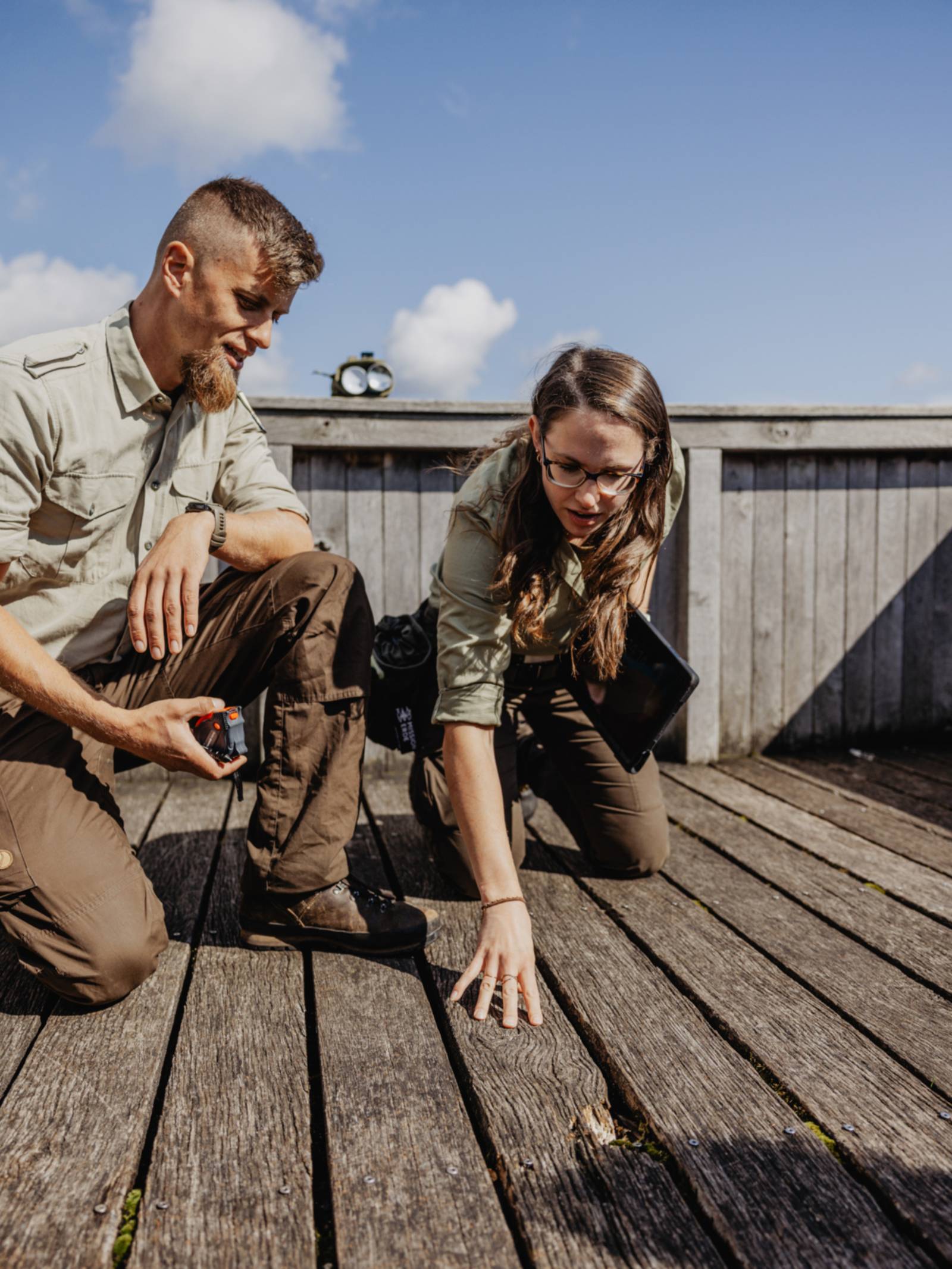 Eine Rangerin und ein Ranger knien auf einem Holzboden und begutachten die groben Dielen.