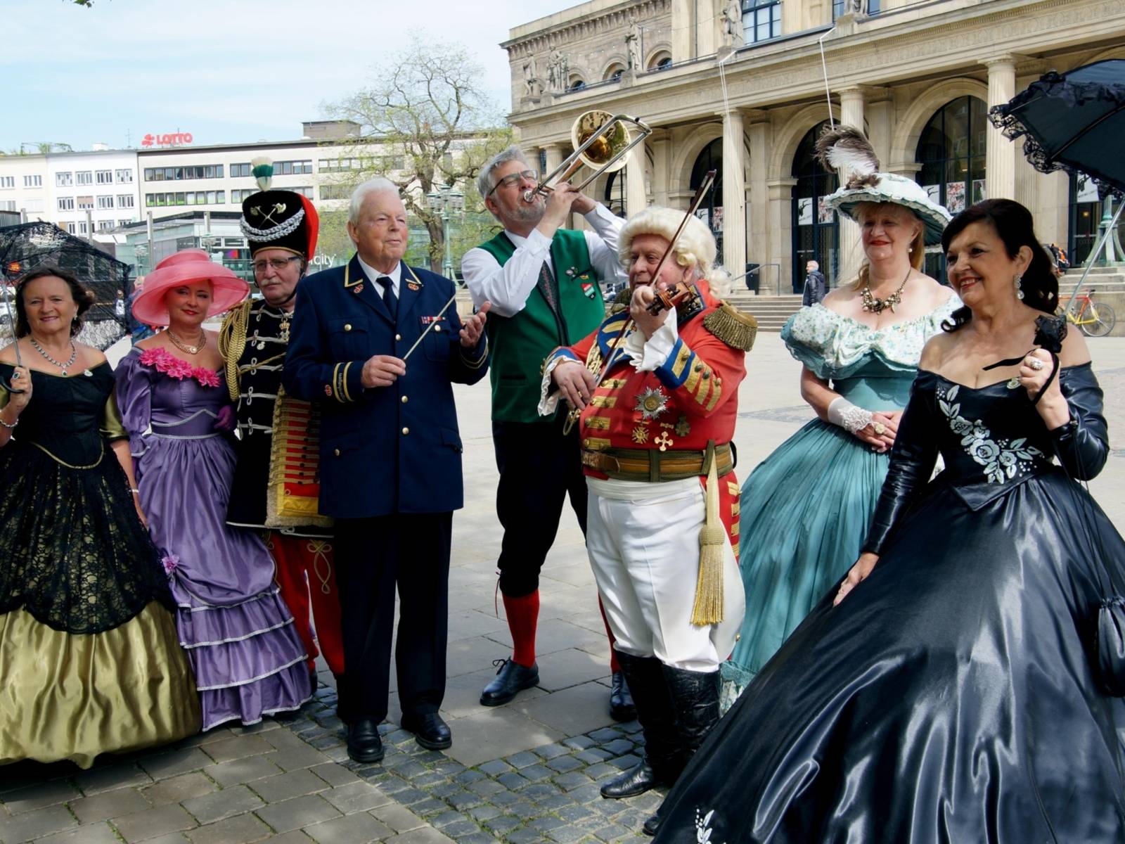 Vier Männer und vier Frauen in historischen Kostümen vor einem Gebäude.