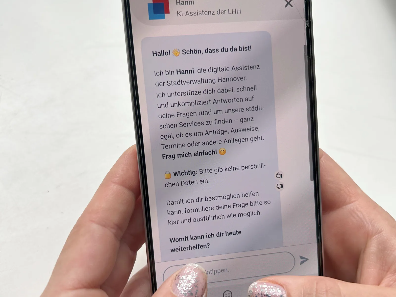 Zwei Hände halten ein Handy in der Hand. Auf dem Handy ist "Hanni" geöffnet, der Chatbot der Landeshauptstadt Hannover.