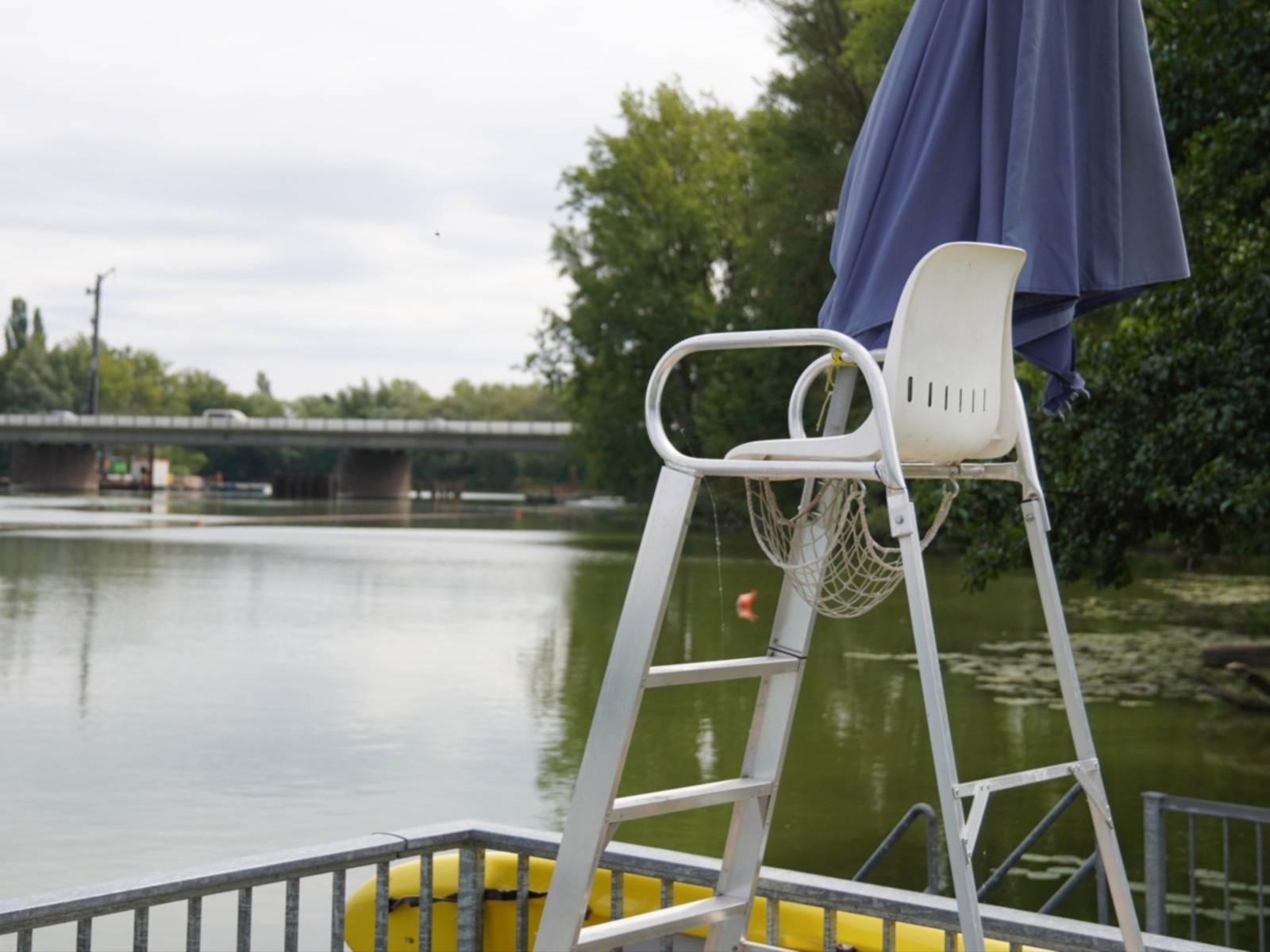 Ein weißer Hochstuhl vor einem See, hinten verläuft eine Brücke mit Autos über den See.