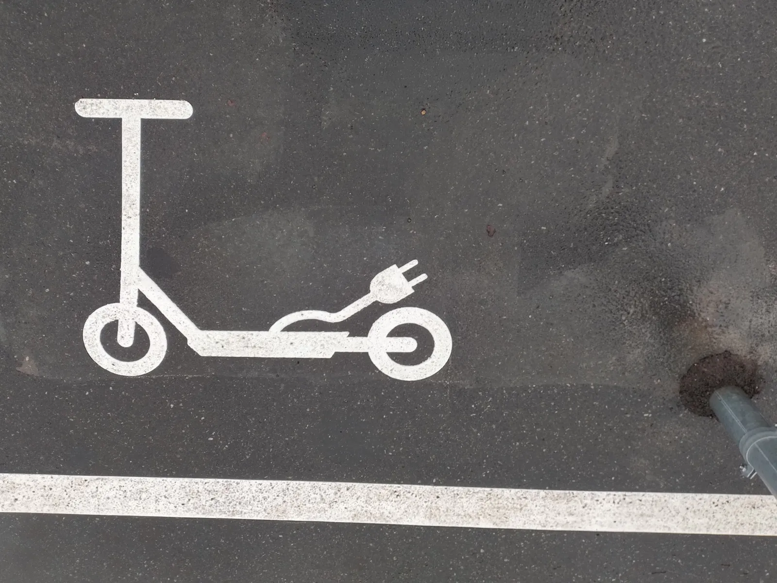 Ein auf Aspalt aufgetragenes weißes Roller-Sybol mit einem Stromstecker, davor ein weißer Streifen als Markierung.