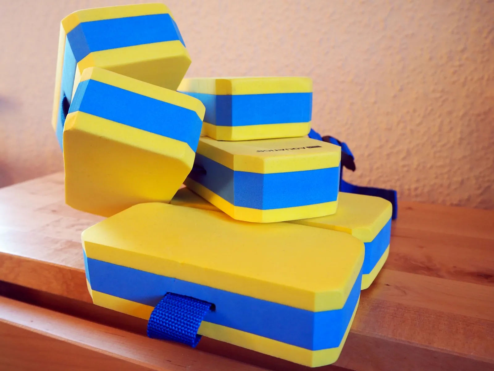 Sechs Auftriebskörper in den Farben Blau und Gelb werden durch einen Gürtel zusammengehalten. Um den Bauch gebunden, kann dieser Schwimmgürtel einem Kind beim Schwimmenlernen helfen.
