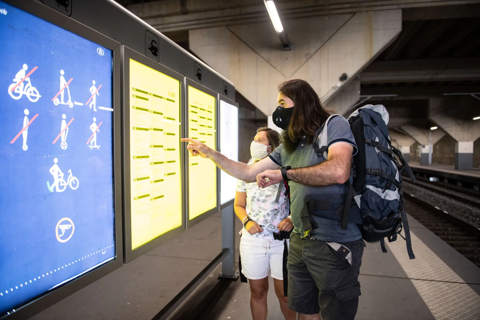 Passengers with face masks looking at the train schedule
