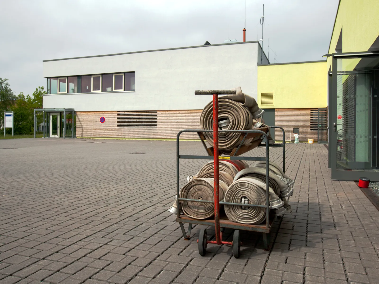 Auf einem Handkarren liegen Feuerwehrschläuche, im Hintergrund ist die Feuerwehrtechnische Zentrale (FTZ) Burgdorf