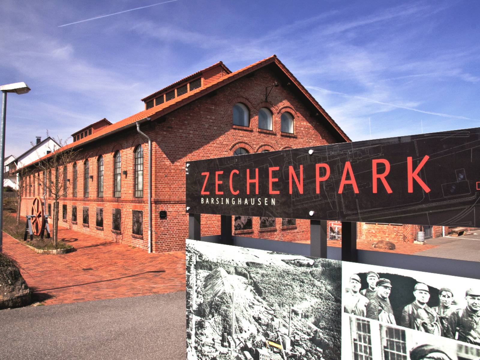 Schild mit der Aufschrift "Zechenpark. Barsinghausen", dahinter ist ein Backsteingebäude.