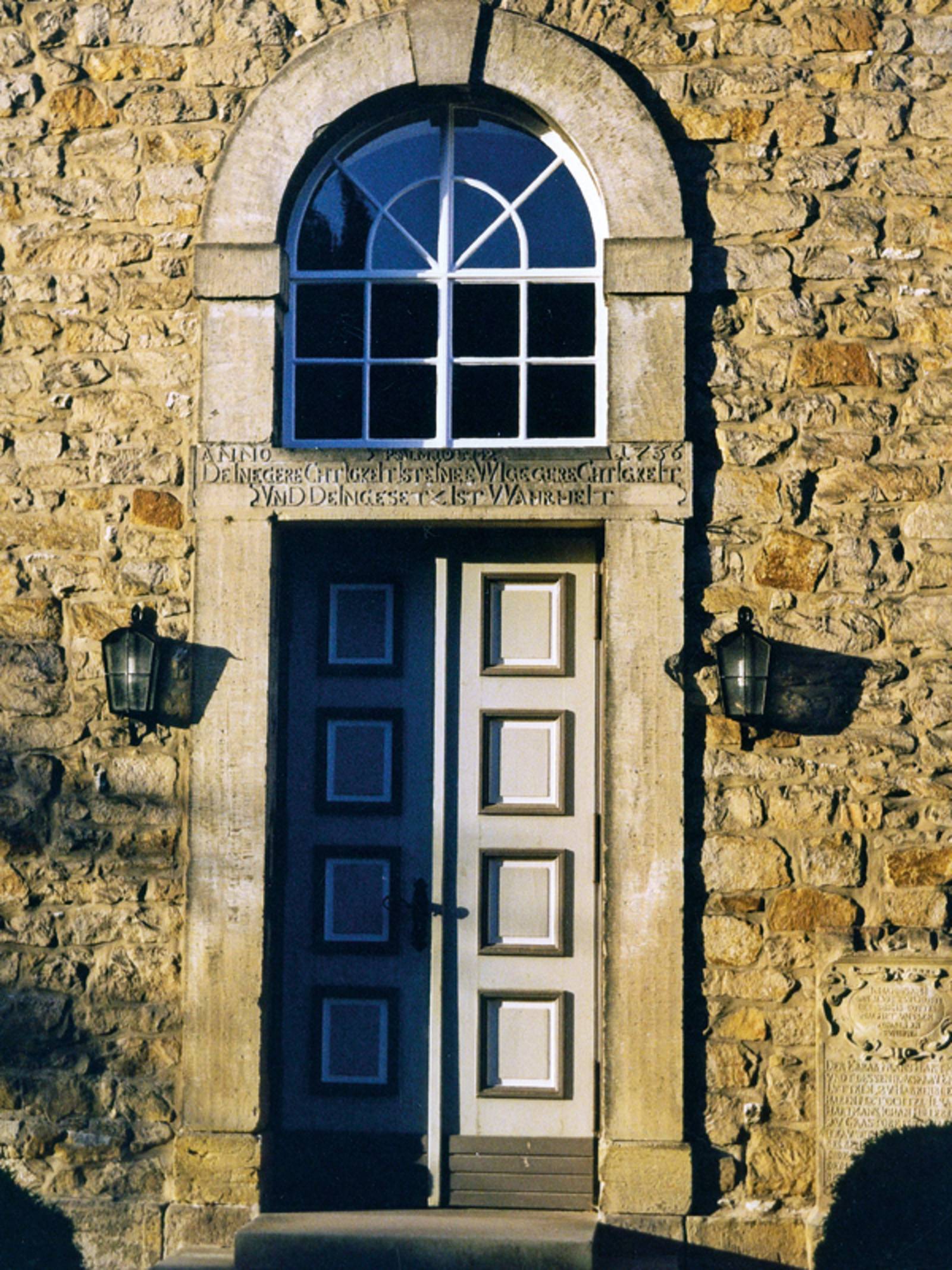 Hohe alte Tür mit einem Rundbogenfenster über dem Türzsturz in einem aus Bruchsteinen gemauerten Gebäude