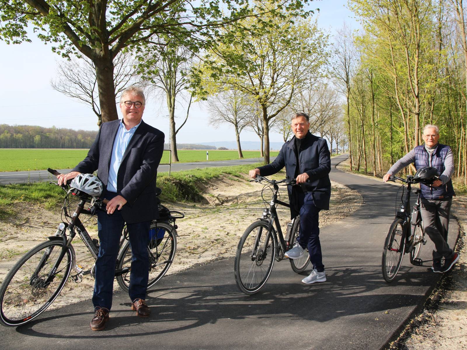Drei Herren mit Fahrrädern auf einem neuen Radweg