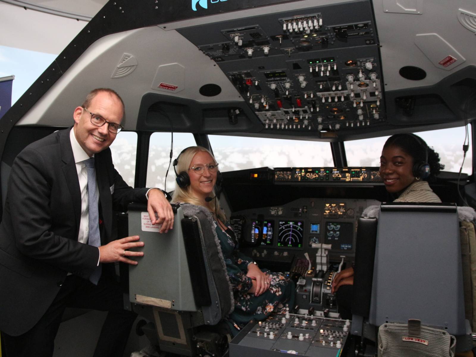 Zwei junge Frauen und ein Mann in einem Flugsimulator.