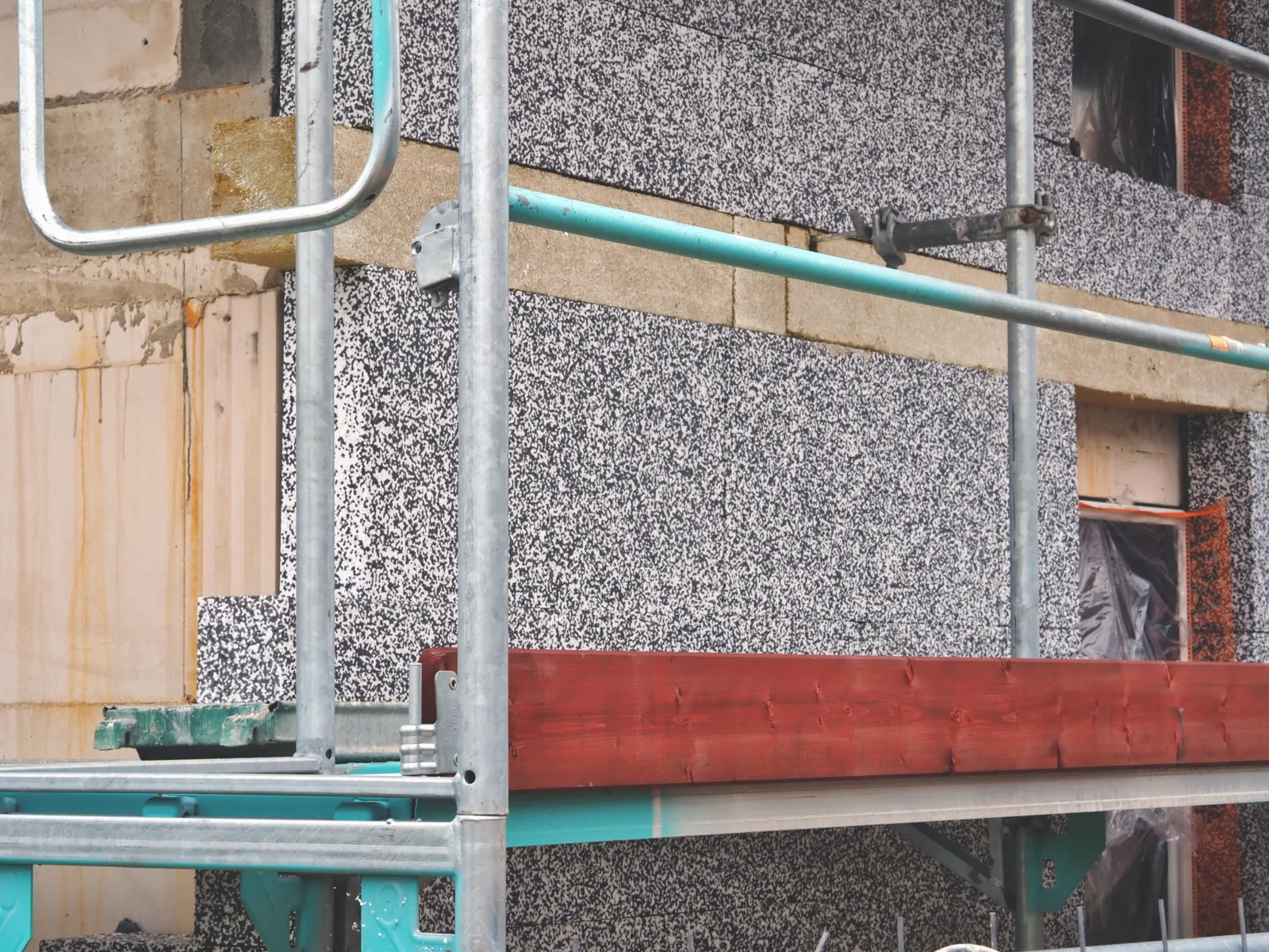 Ein Gerüst steht an einem Rohbau, an die Fassade wird Wärmedämmung angebracht.  