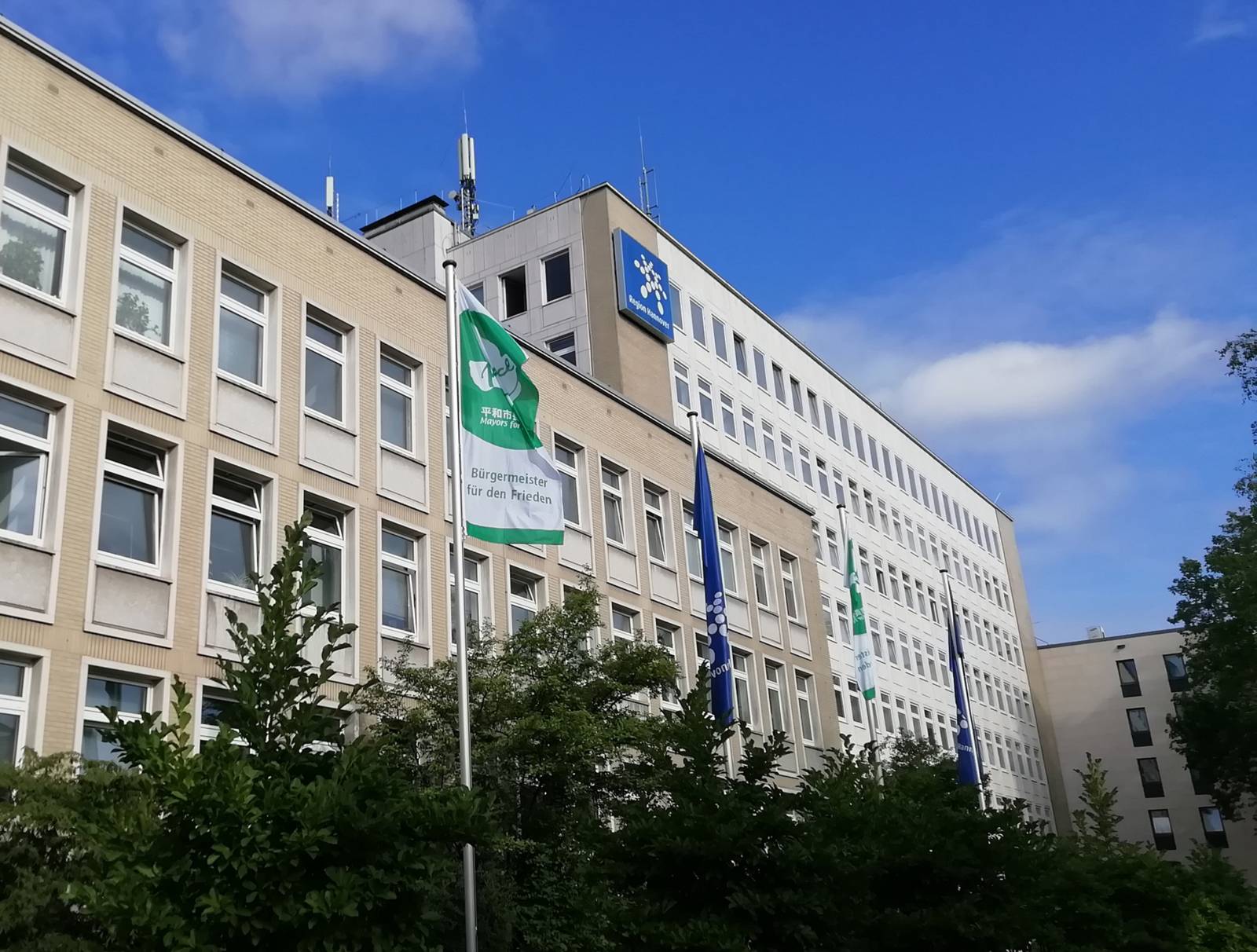 Ein großes Verwaltungsgebäude von außen mit Flaggen und Bäumen davor.