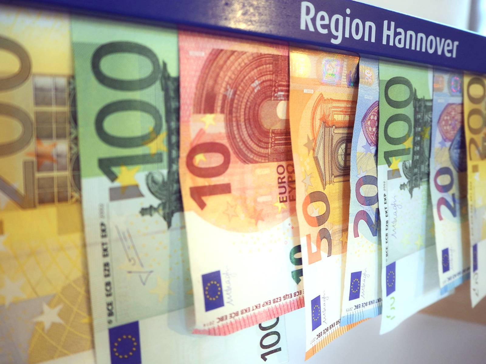 Geldscheine hängen von einem blauen Holzstück, auf dem "Region Hannover" steht.