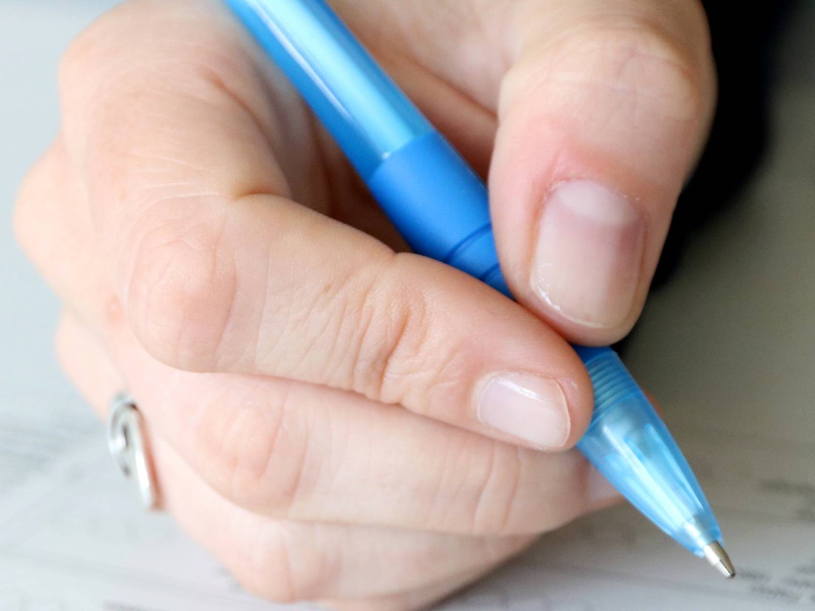 Eine Hand hält einen blauen Kugelschreiber und bewegt sich über ein Formular.