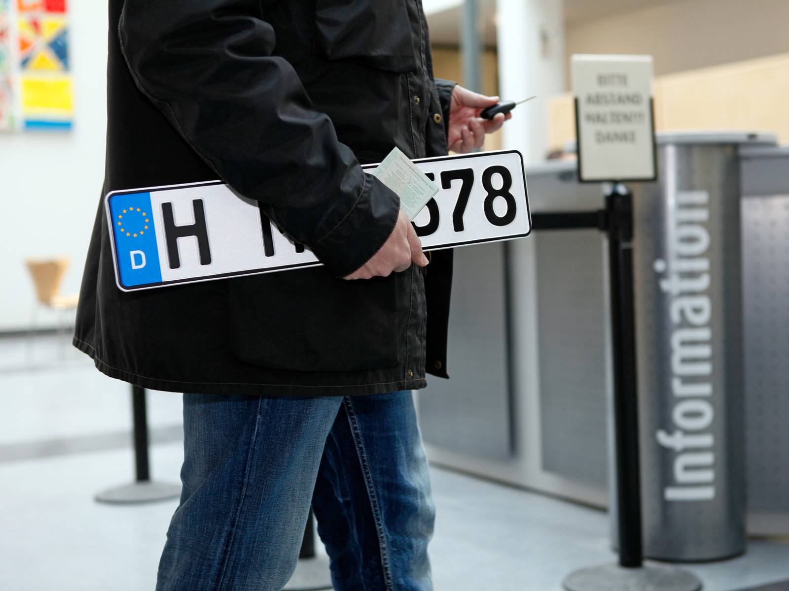 Eine Person mit einem KFZ-Kennzeichen unter dem Arm auf dem Weg zur Informationsstelle