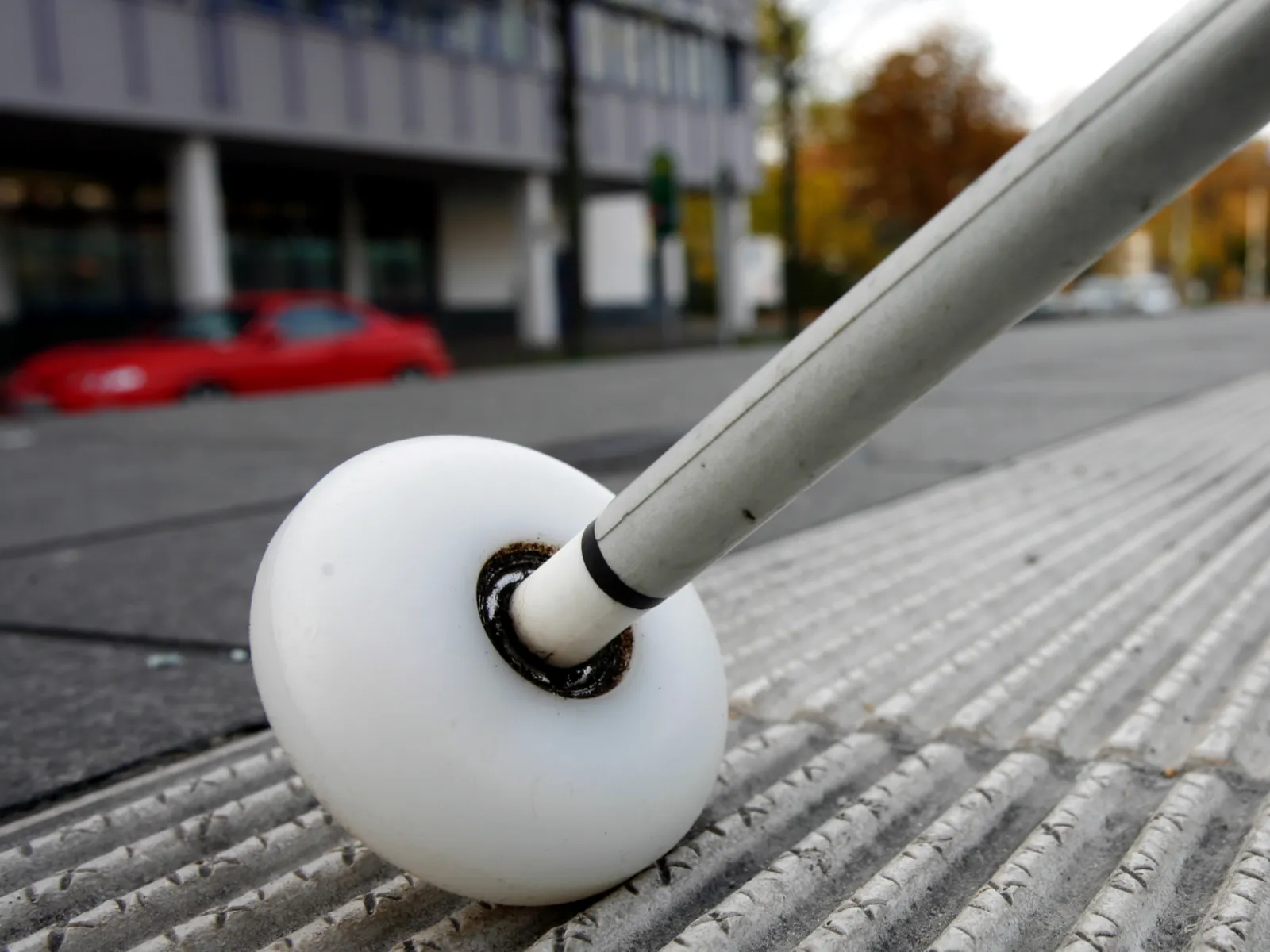 Ein weißer Langstock mit rollender Kugelspitze wird über ein Rillenplattensystem geführt.