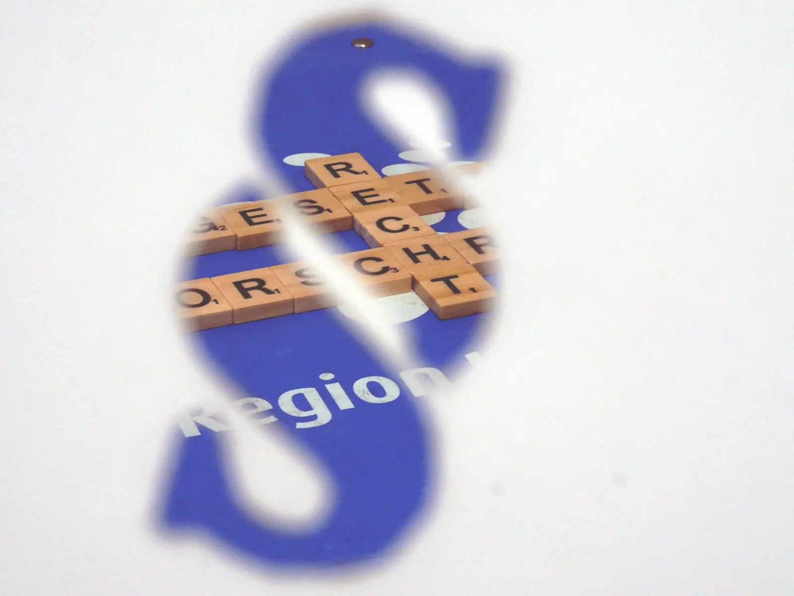 Blick durch einen Paragrafen: Bausteine mit Buchstaben liegen auf einem blauen Hintergrund, sie bilden die Worte "Recht", "Vorschrift" und "Gesetz". 