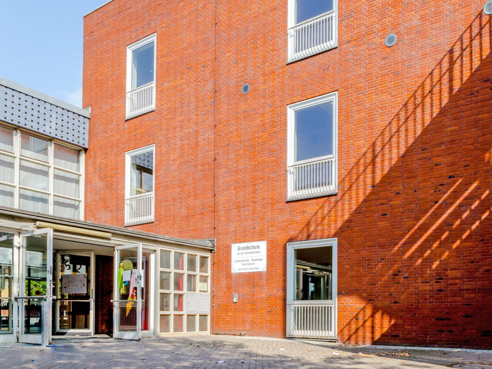 Am Eingang zur Grundschule An der Uhlandstraße sind Schultüten in Papierform an die Türen geklebt, die offen stehen. Die Schule ist in einem mehrstöckigen Backsteinbau untergebracht.