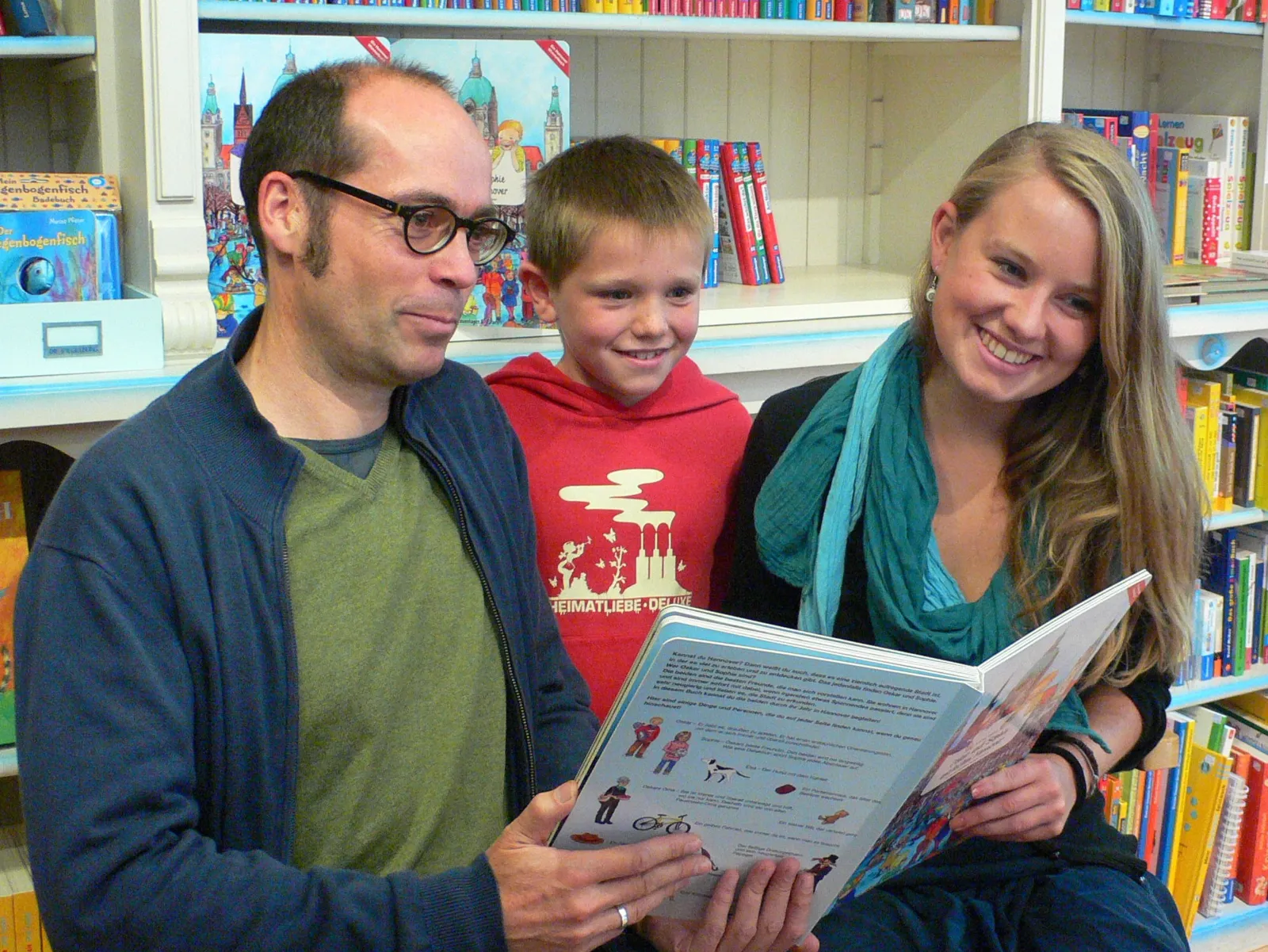 Ein Mann, ein Junge und eine Frau halten ihr Buch lächelnd in die Kamera.