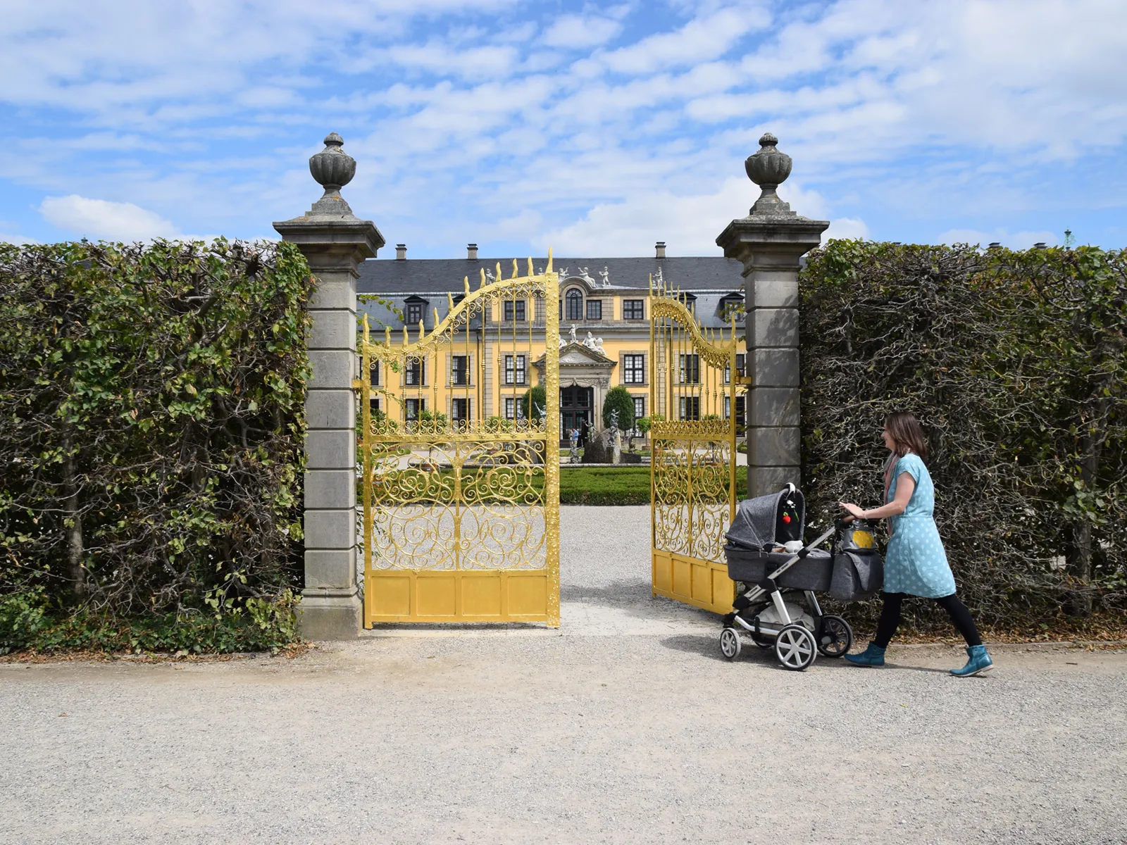 Eine Frau schiebt einen Kinderwagen durch ein goldenes Tor