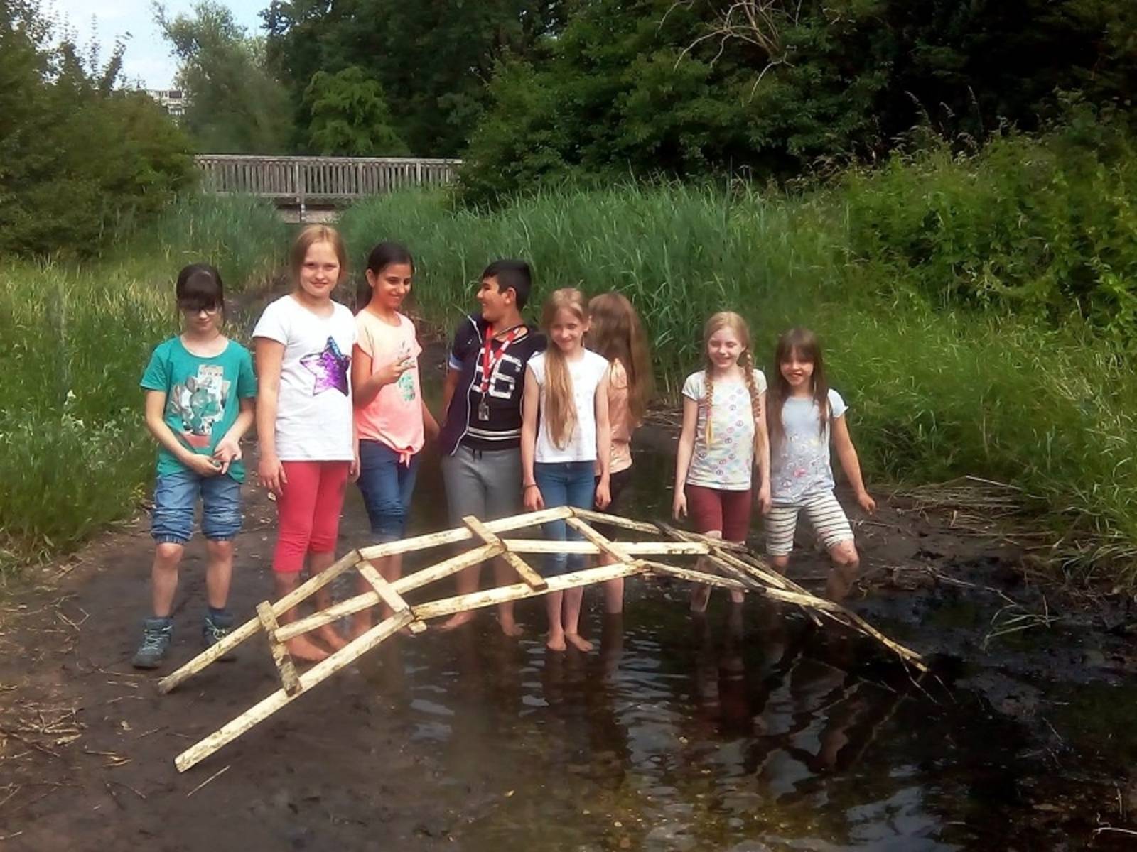 Eine Gruppe von Kindern, die in einem Bach stehen mit einer selbstgebauten Brücke.