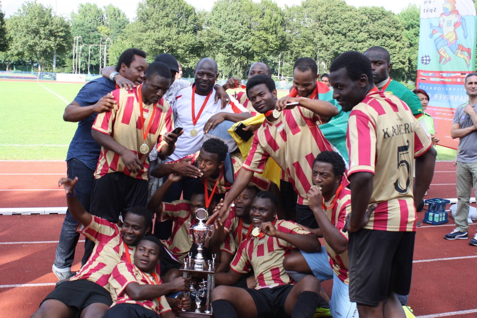 15 Spieler des Team Kamerun feiern ausgelassen den Titelgewinn und posieren mit dem Pokal für ein Foto.