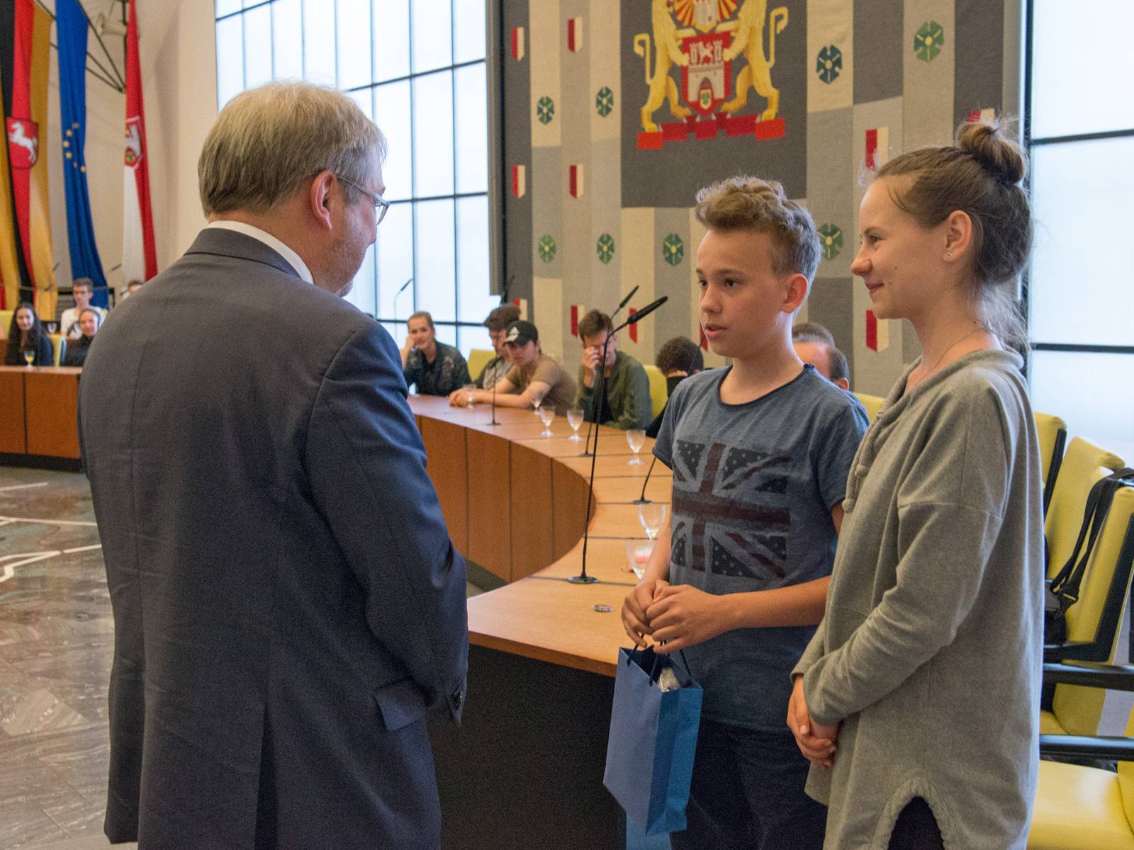 Zwei Jugendliche übergeben eine Geschenktasche an Bürgermeister Hermann
