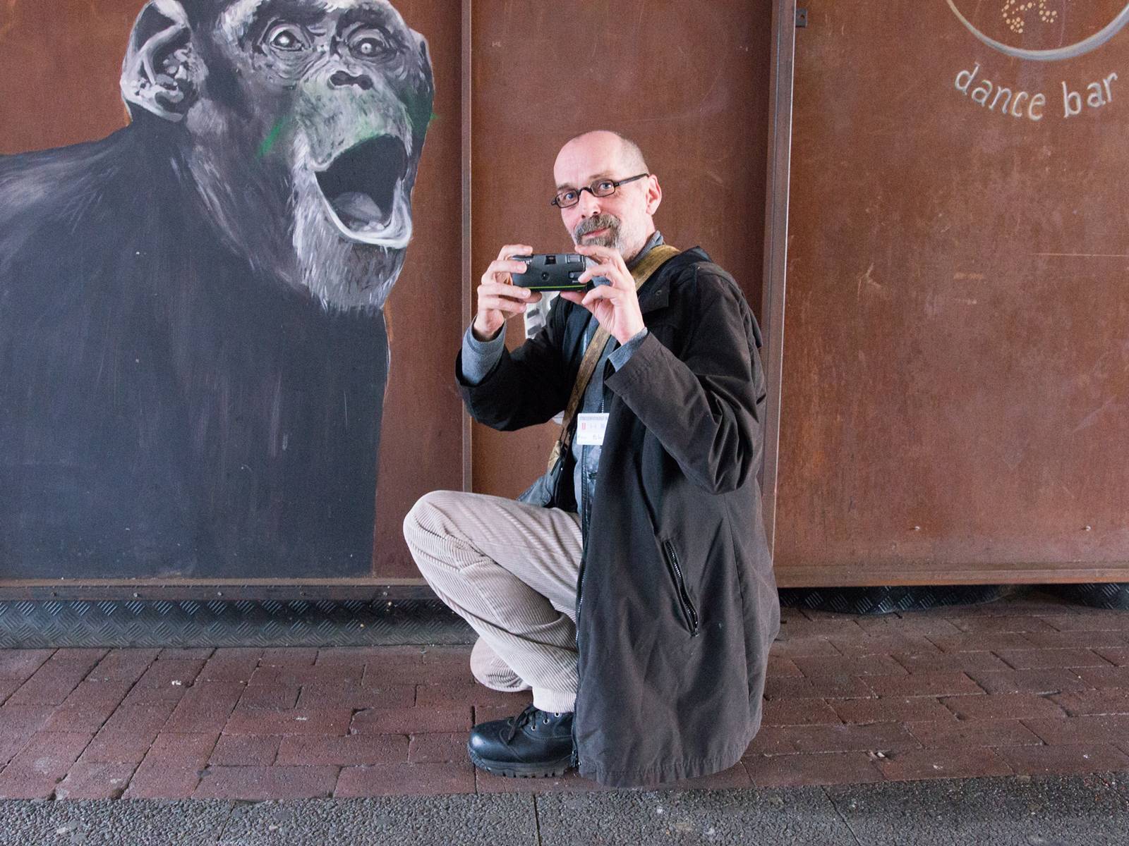 Ein Mann hält eine Fotokamera in der Hand und kniet vor einer Wandmalerei