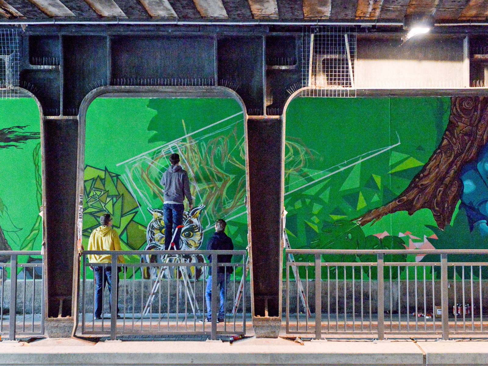 Drei Menschen die ein Graffiti an die Wand einer Unterführung malen. 