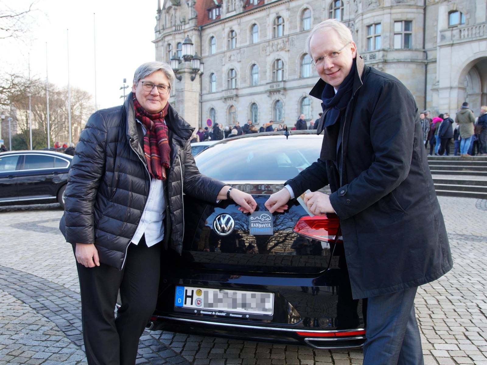 Eine Frau und ein Mann, die eine Plakette an einem Auto anbringen. 