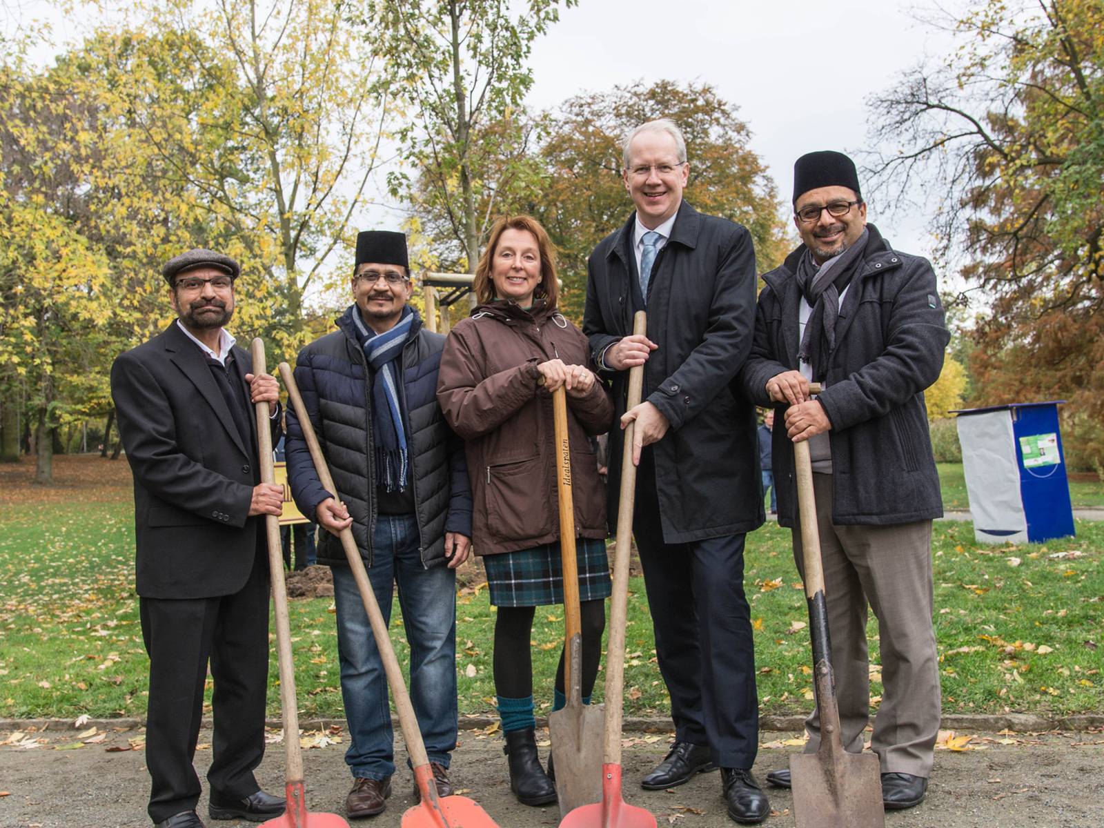 Fünf Personen mit Schaufeln vor einem neu gepflanzten Baum