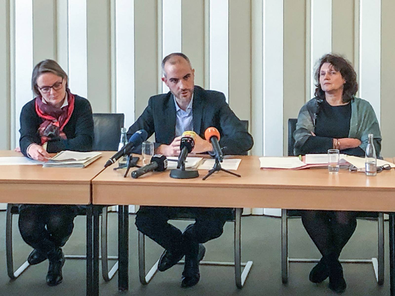 Drei Personen sitzend an einem Tisch während einer Pressekonferenz