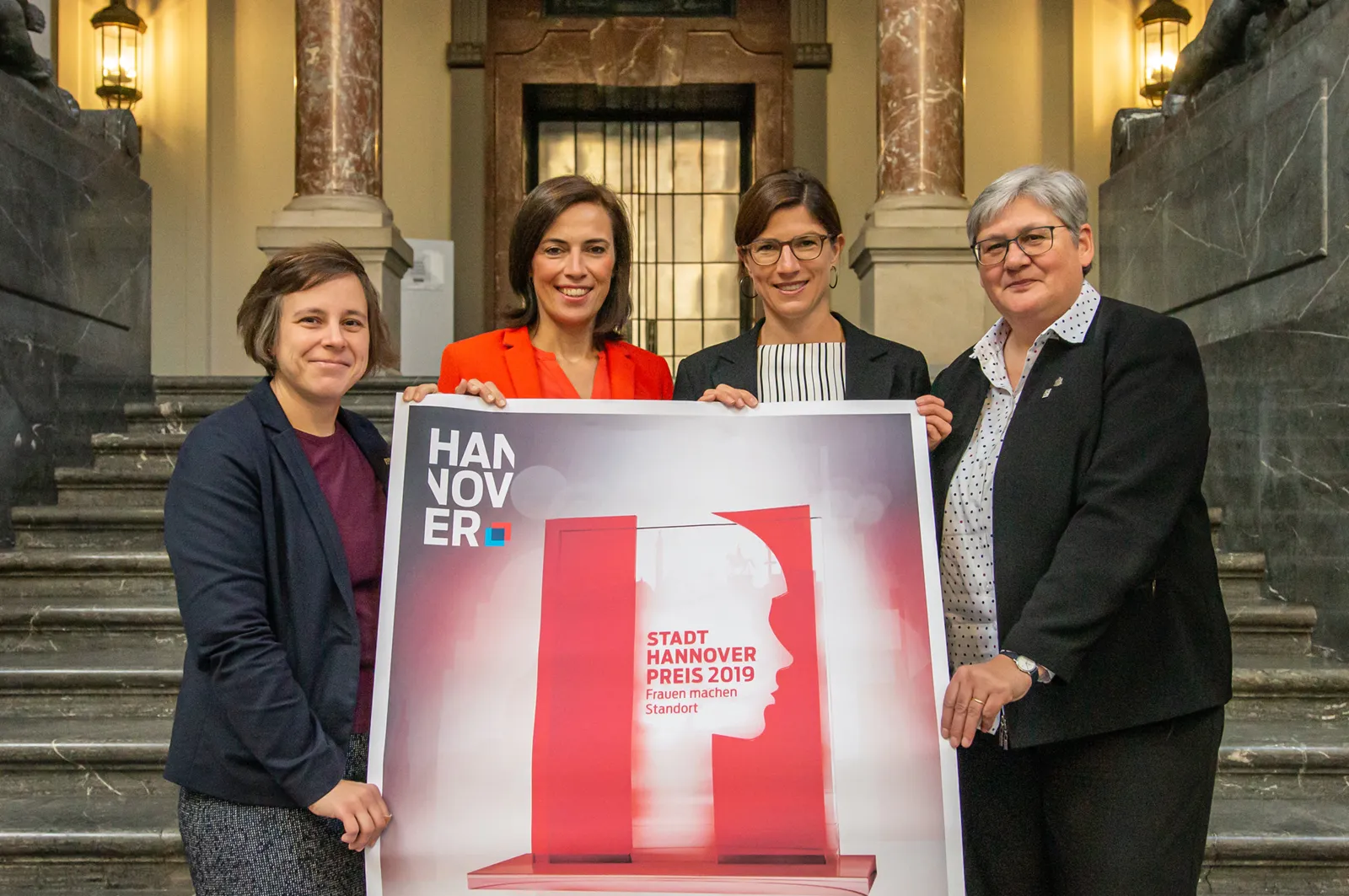 Vier Personen mit einem Plakat in einer Halle. 