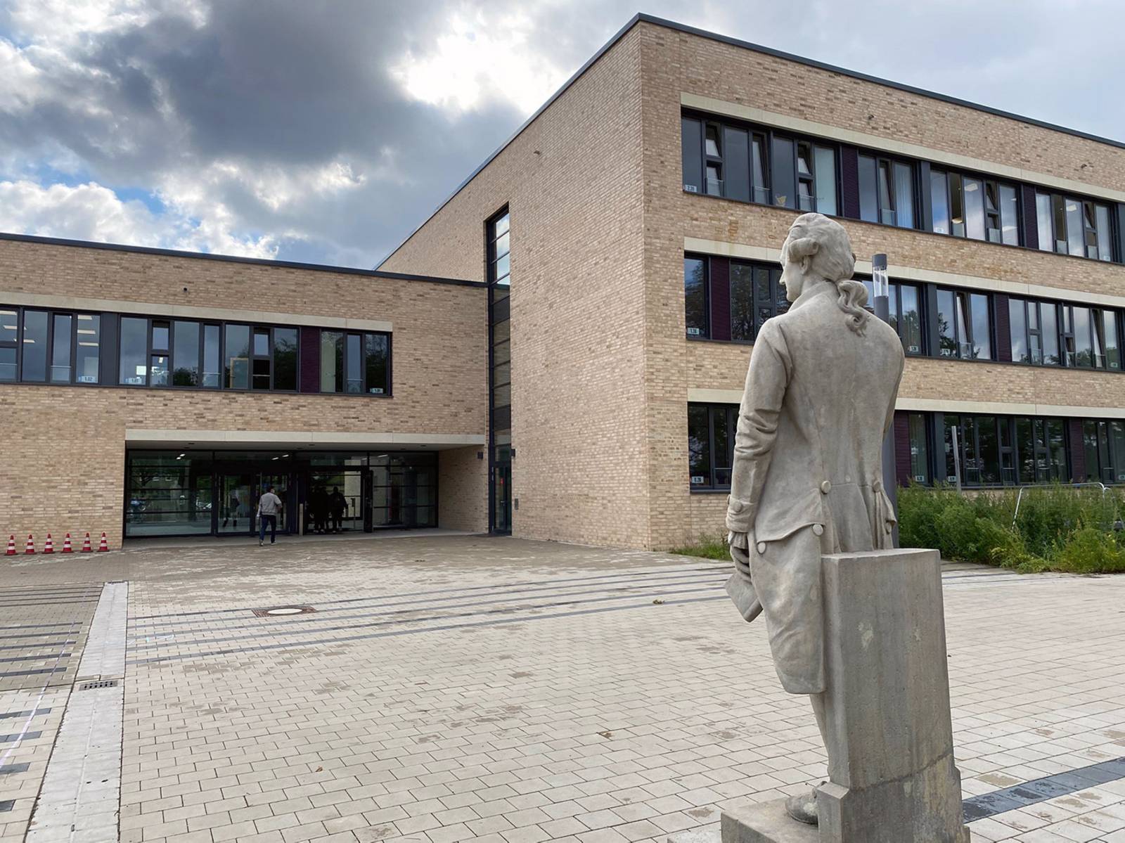 Ein modernes Schulgebäude, rechts davor eine Statue.
