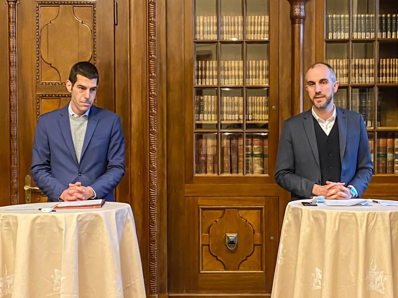 Zwei Männer stehen während einer Pressekonferenz jeweils an einem tisch