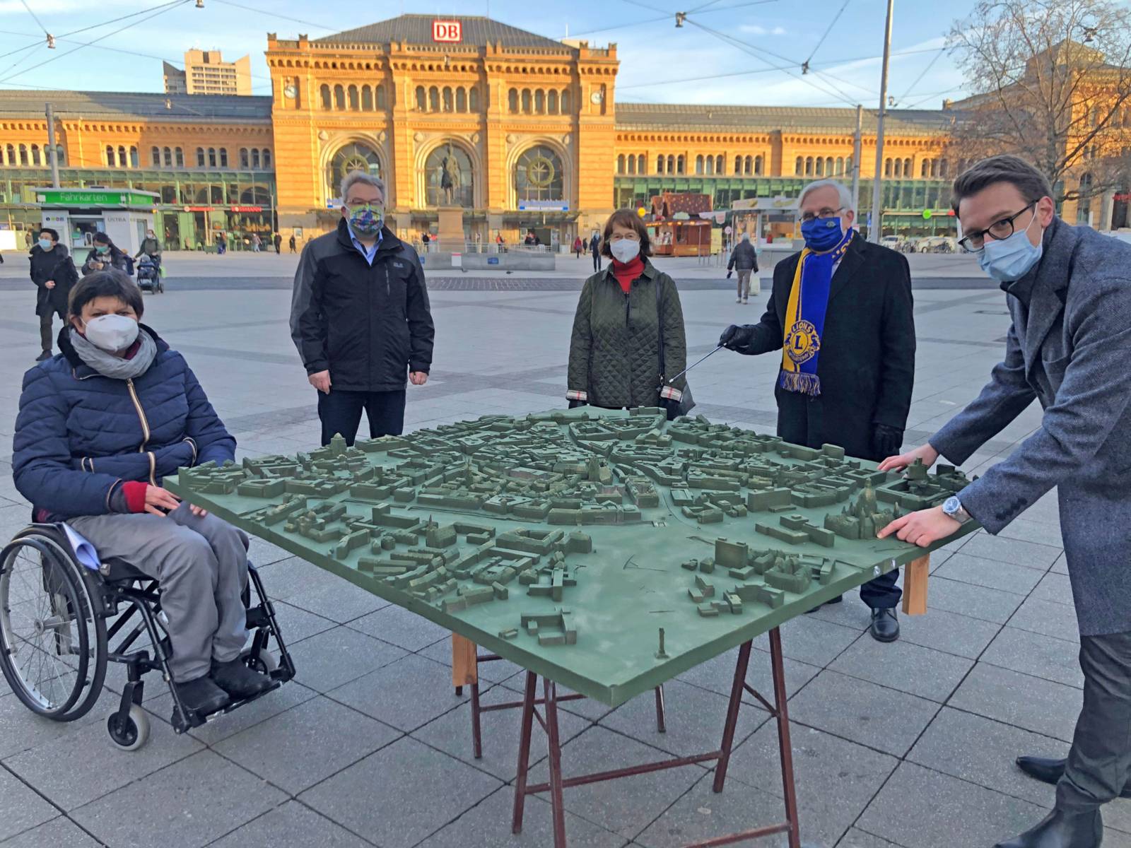 Fünf Personen um ein großes Stadtmodell. Alle halten Abstand und tragen einen Mund-Nasen-Schutz. 