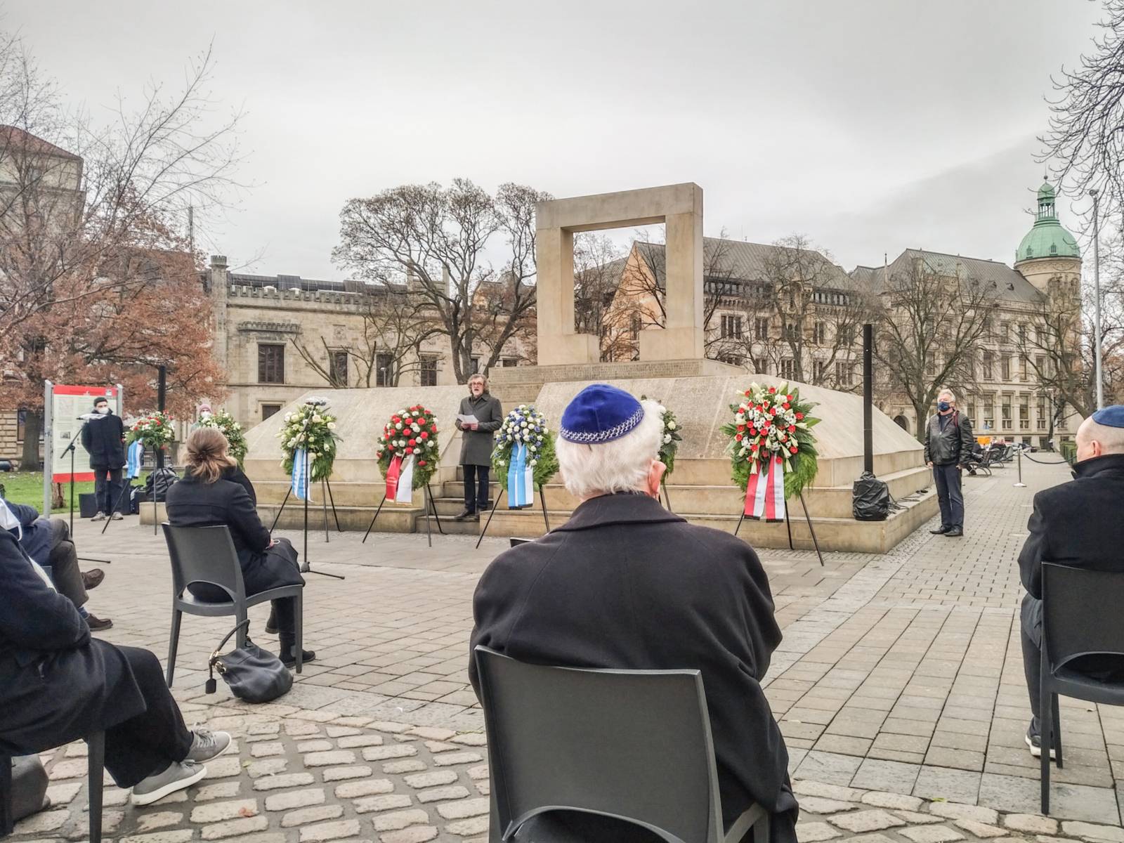 Eine Gruppe Personen sitzt mit Abstand vor dem Holocaust-Mahnmal
