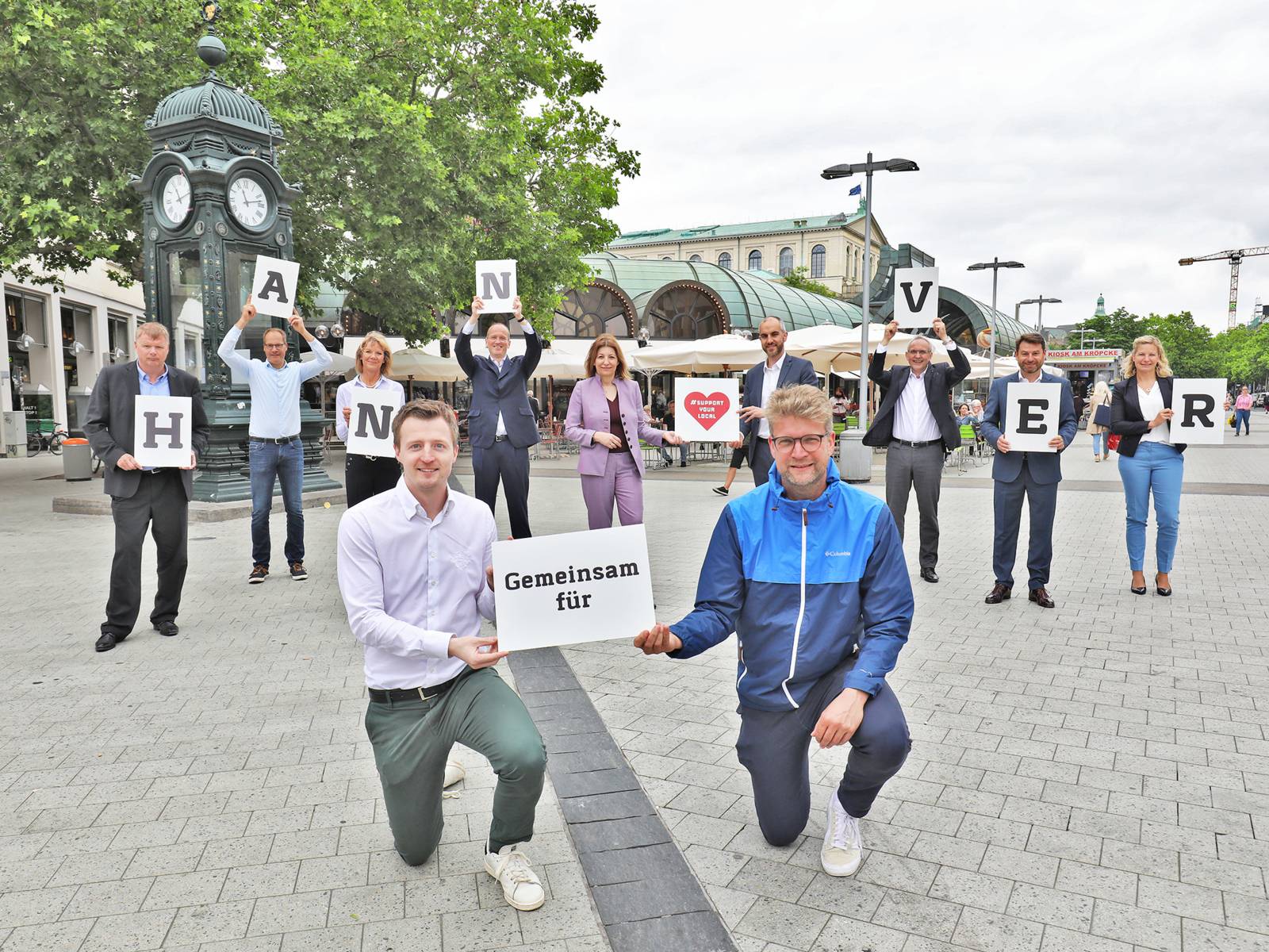 Elf Personen stehen auf einem Platz und bilden mit Schildern den Schriftzug "Gemeinsam für Hannover"