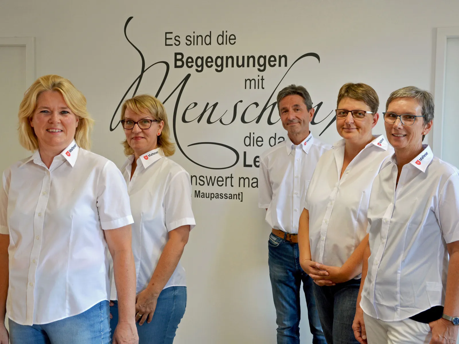 Vier Frauen und ein Mann stehen vor einer Wand, auf der ein Zitat von Guy de Maupassant steht: "Es sind die Begegnungen mit Menschen, die das Leben lebenswert machen".