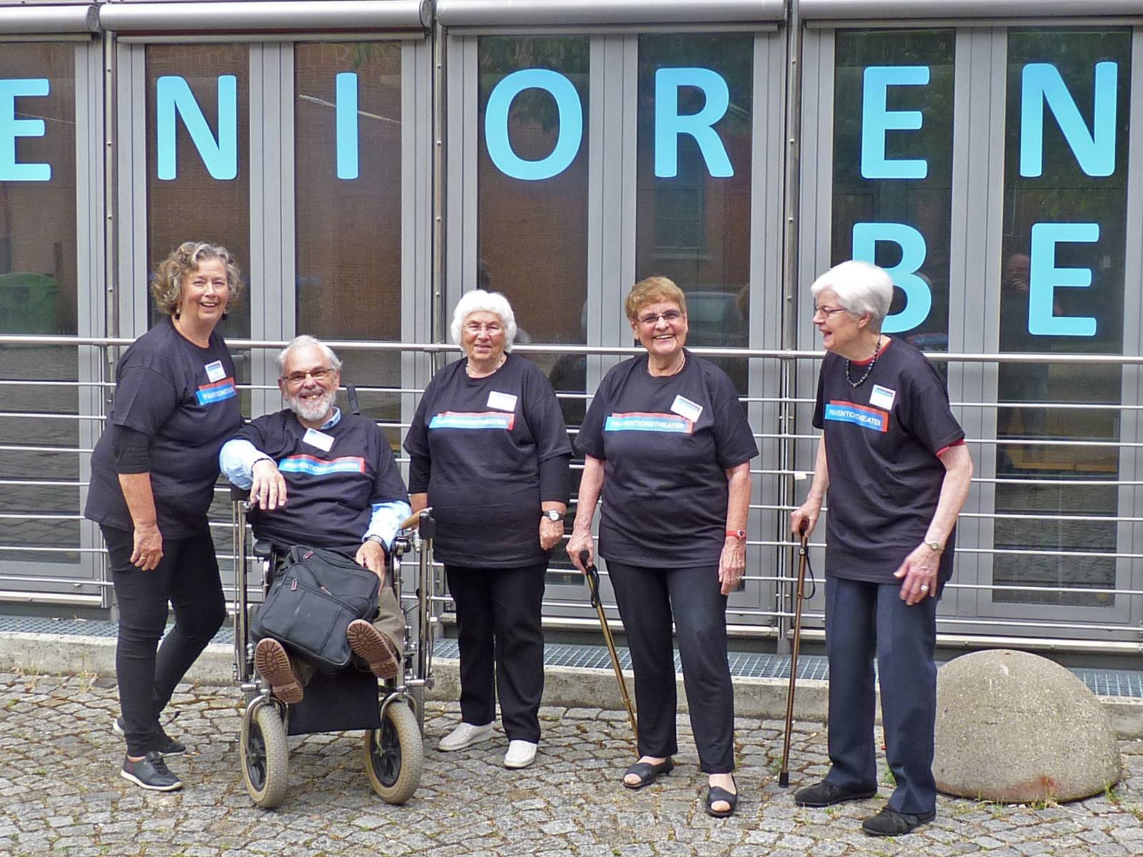 Gruppenaufnahme von vier älteren Damen und einem älteren Herrn, die jeweils T-Shirts mit der Aufschrift "Präventionstheater" tragen.