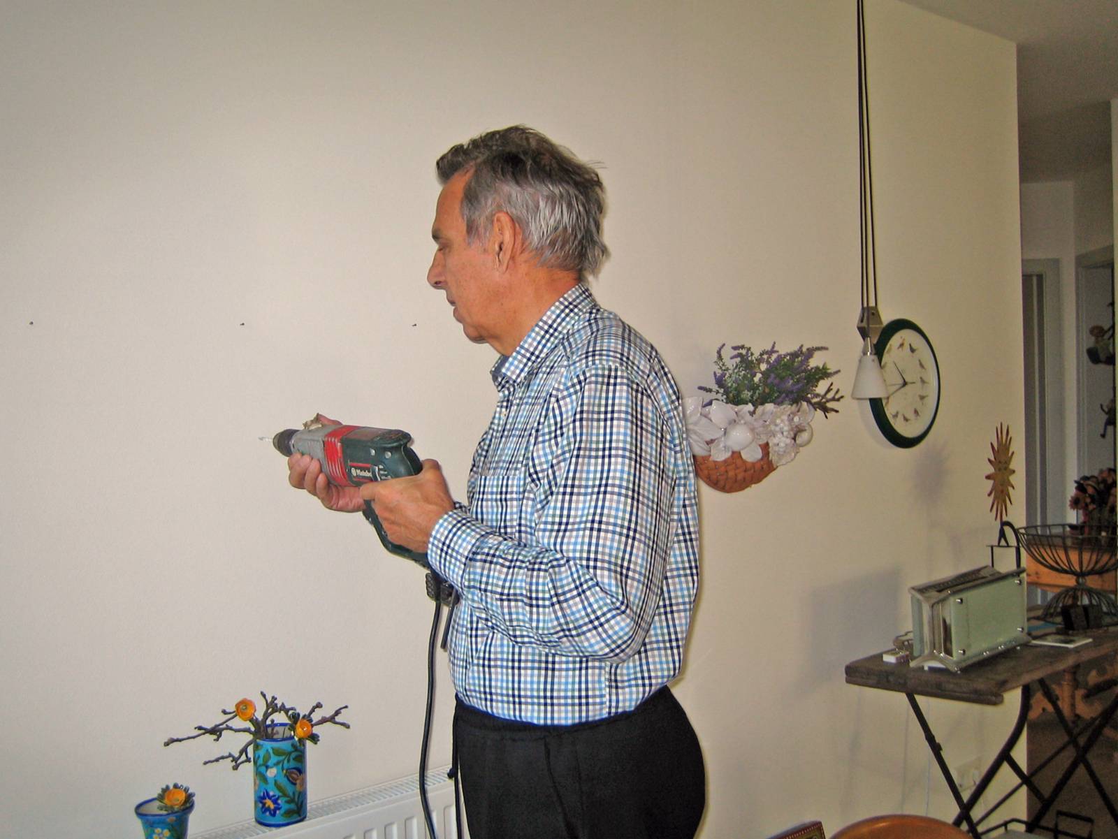 Ein älterer grauhaariger Mann bohrt ein Loch in eine Wand