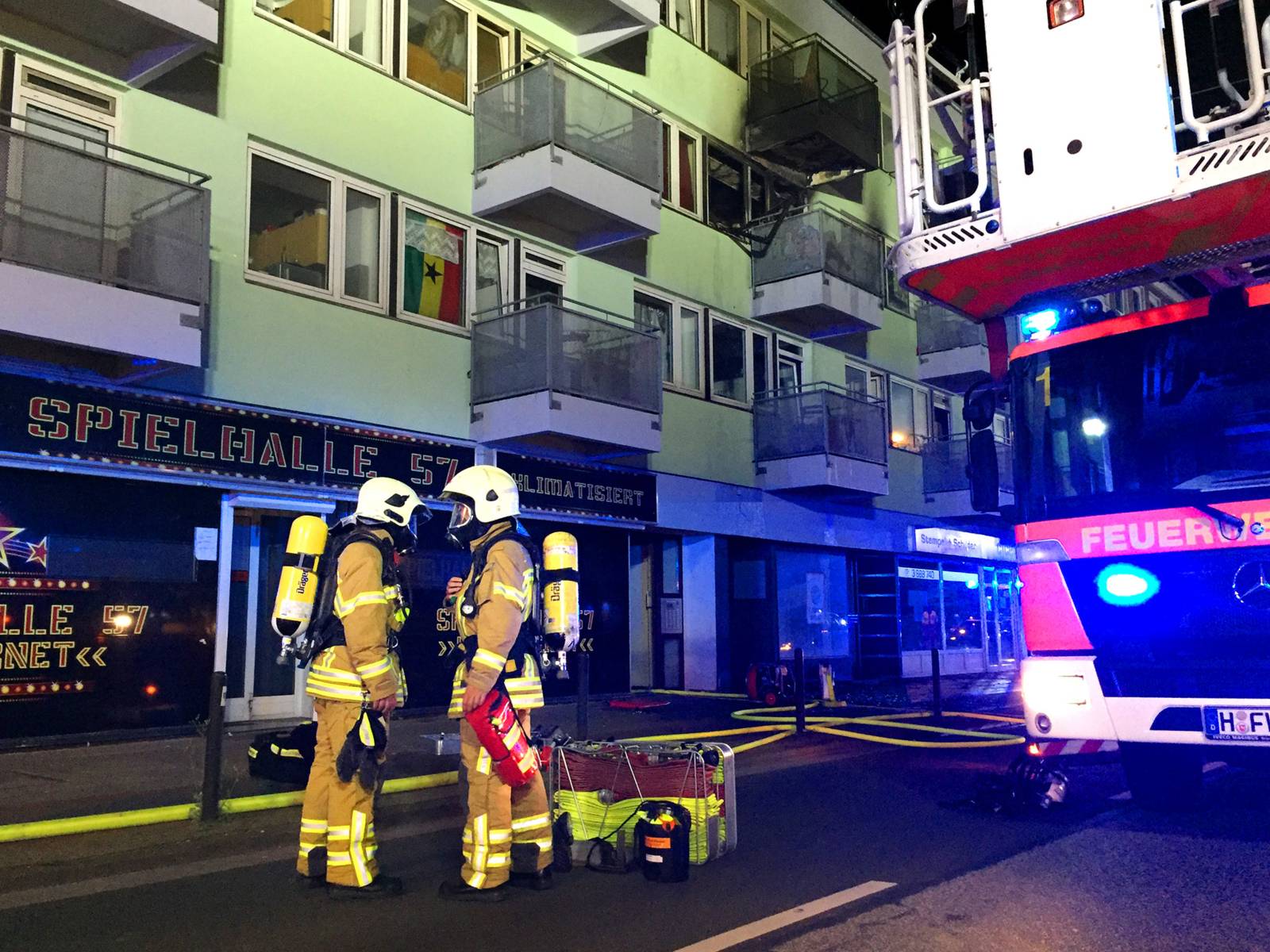 Zwei Einsatzkräfte mit angelegtem Atemschutz. Im Hintergrund der ausgebrannte Balkon der betroffenen Wohnung.