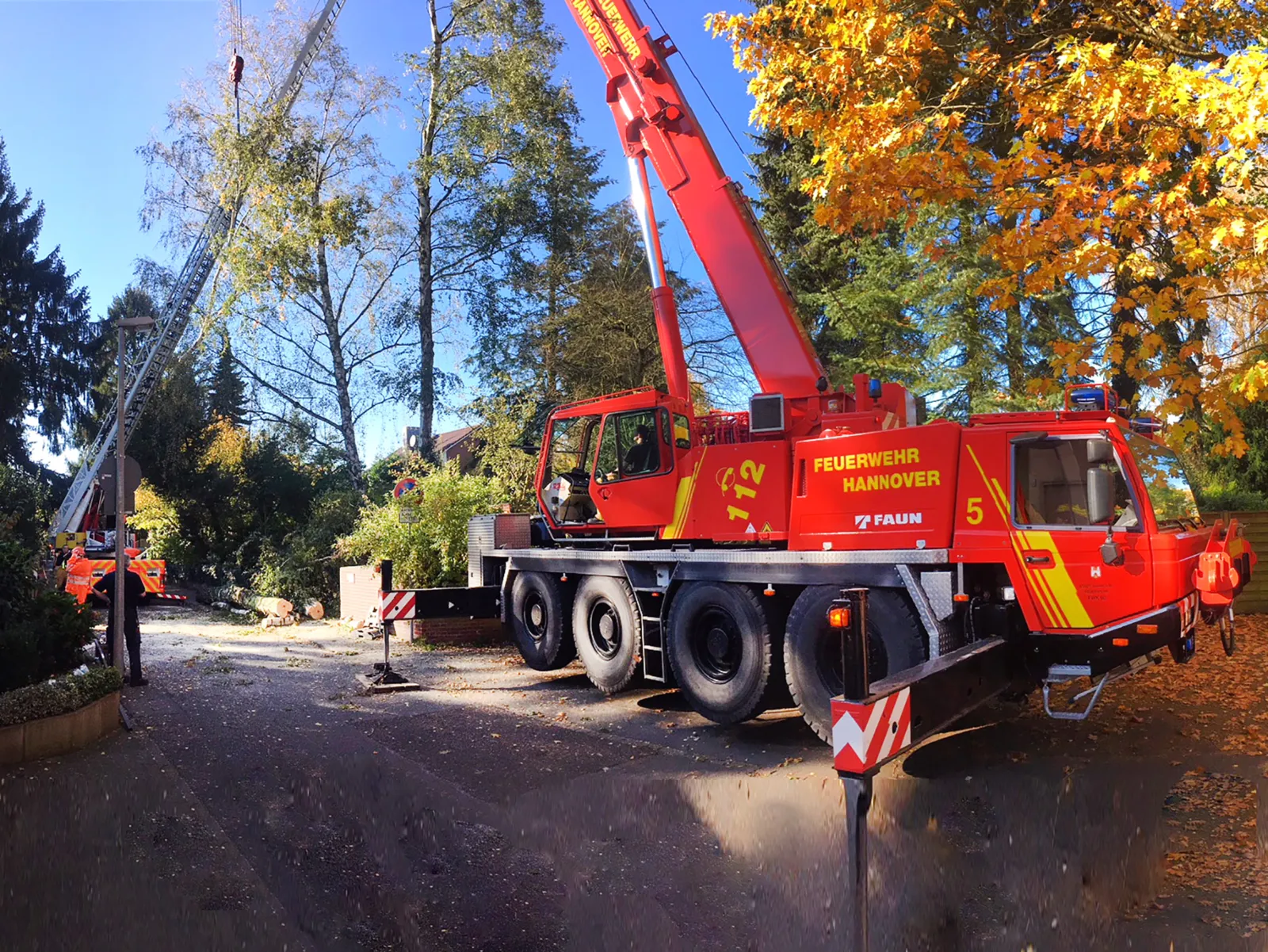 Im Vordergrund ein Kran der Feuerwehr Hannover, im Hintergrund eine Drehleiter mit Einsatzkräften der Feuerwehr Hannover. Die Fahrzeuge stützen den schrägliegenden Baum.