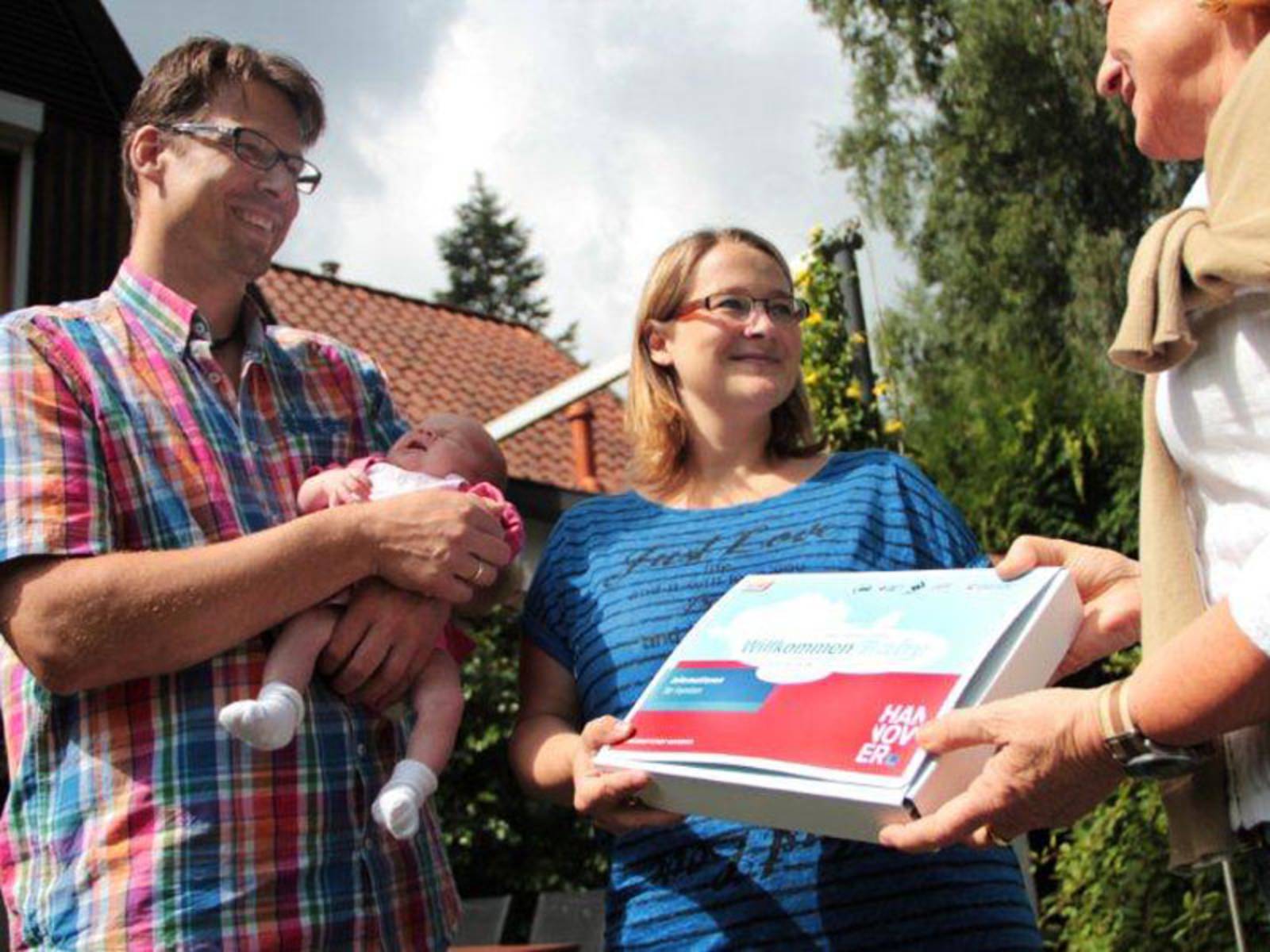 Eltern mit einem Baby auf dem Arm erhalten das Willkommenspaket der Stadt