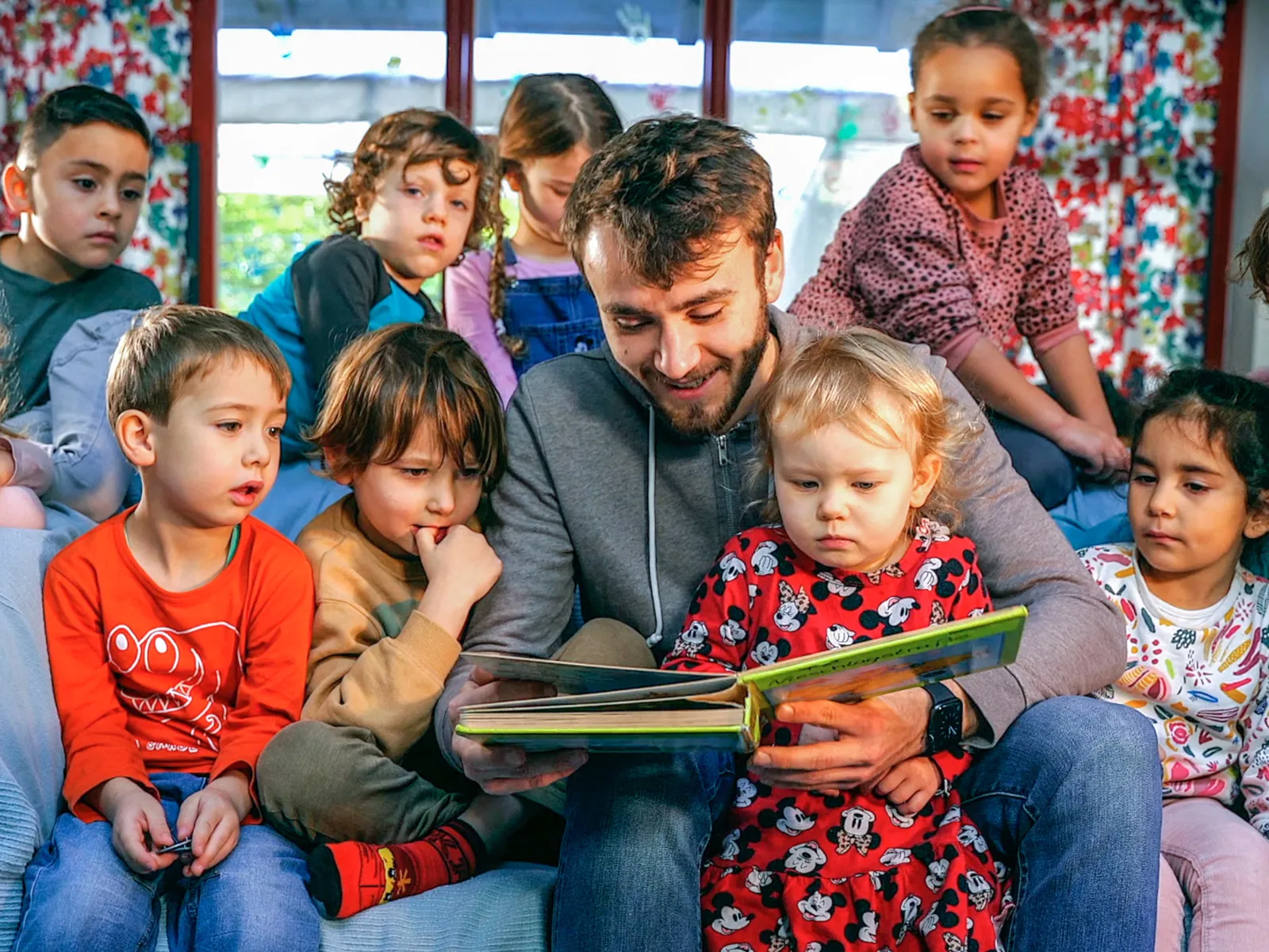Ein Mann sitzt inmitten einer Gruppe Kinder und liest ihnen vor