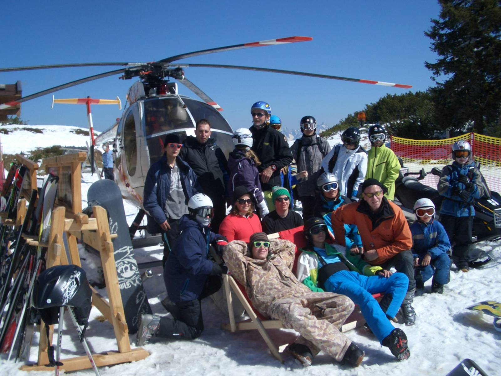 Jugendliche und Ihre Betreuer posieren im Schnee vor blauem Himmel und Helikopter