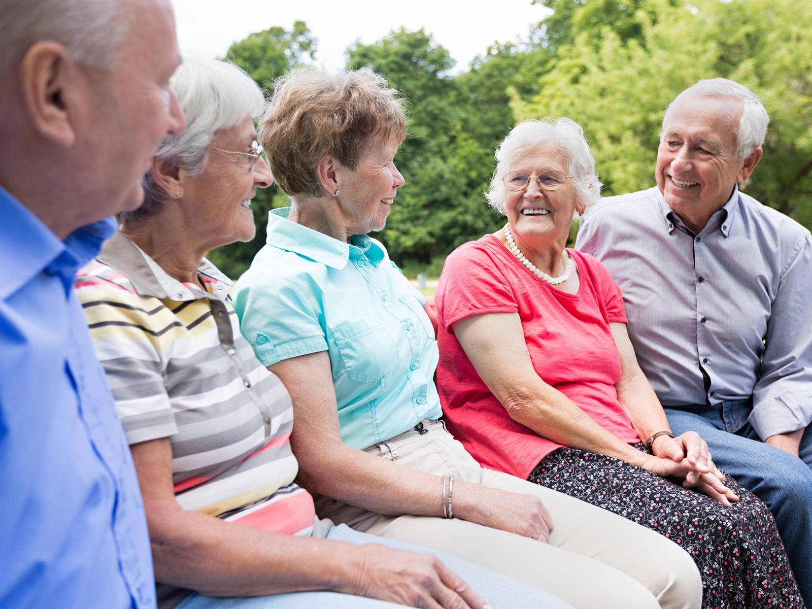 Fünf ältere gut gelaunte Menschen sitzen auf einer Bank im Grünen und lachen gemeinsam