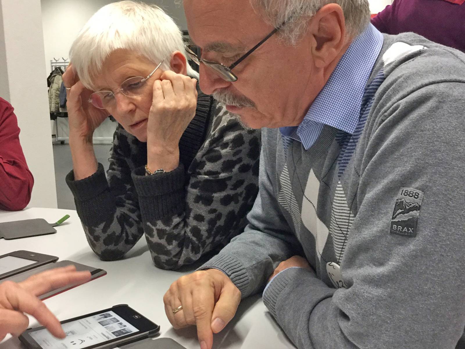 Eine ältere Dame und ein älterer Herr lassen sich die Bedienung eines mobilen Gerätes erklären.