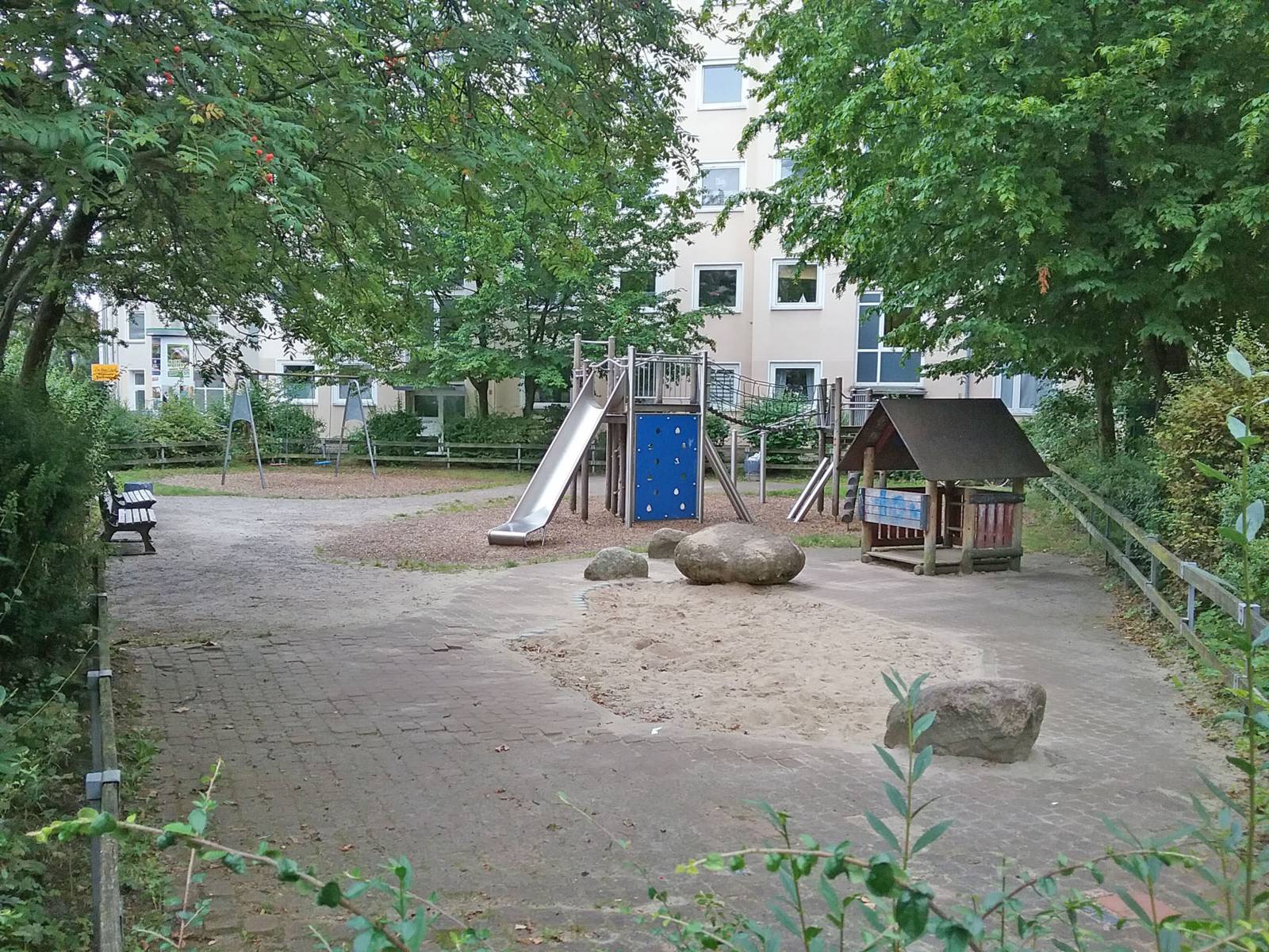 Kleiner Spielplatz mit Rutsche und Klettergerüst, Spielhäuschen, Sandkasten und Schaukel in einem Wohngebiet